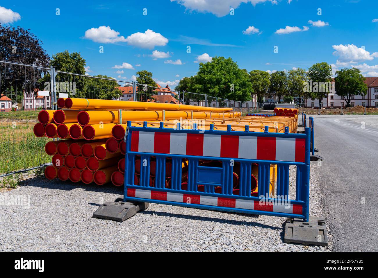 Stack of orang-yellow PVC conduit pipes behind the plastic portable barrier.  Construction site in city. Stock Photo
