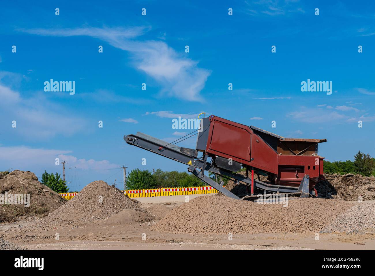 Construction machine with conveyor belt for loading bulk materials. Construction site fenced with yellow plastic barriers. Stock Photo