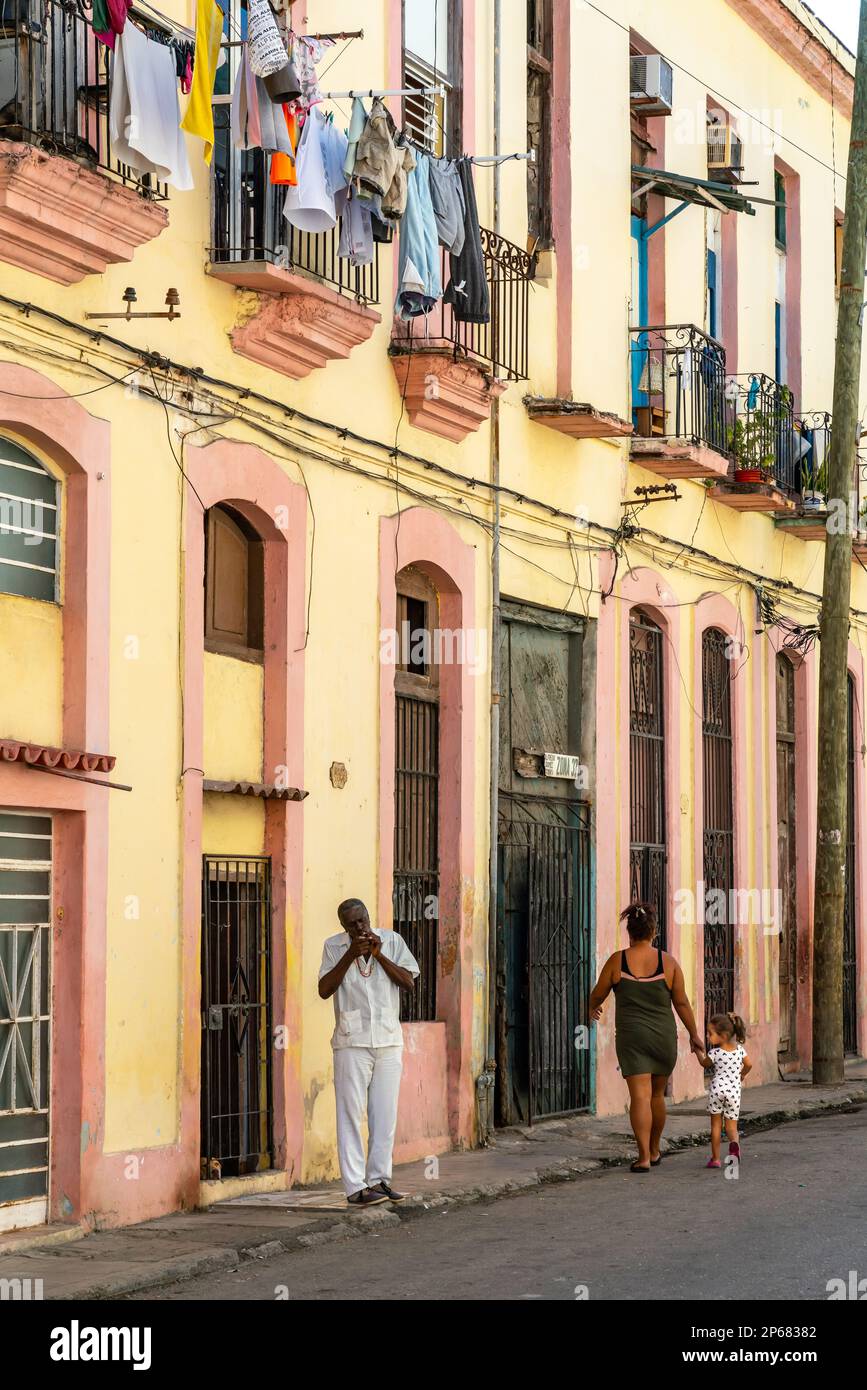 Man lights cigar in typical backstreet, colourful washing draped on balconies, Old Havana, Cuba, West Indies, Caribbean, Central America Stock Photo