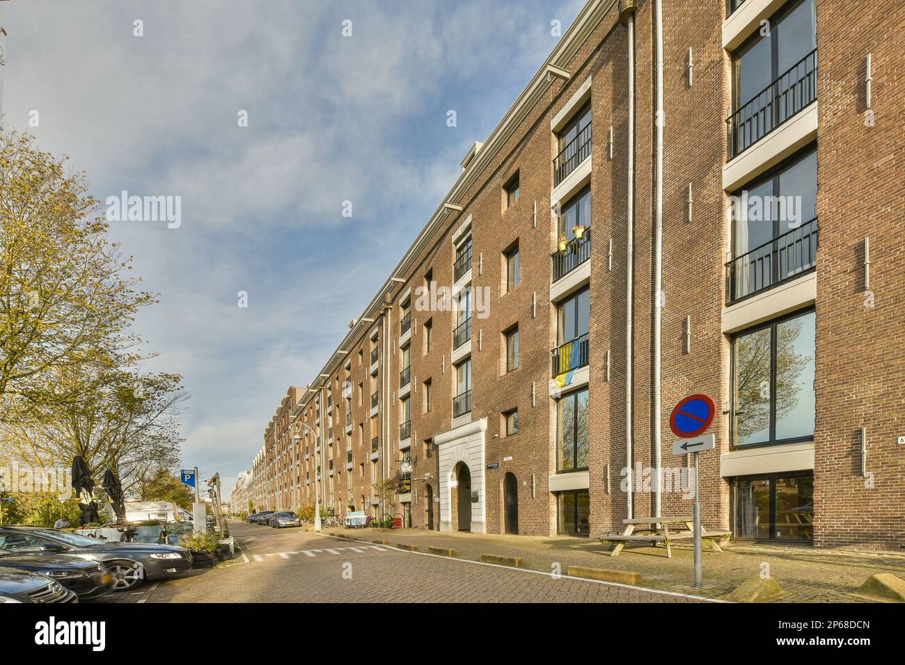 Amsterdam, Netherlands - 10 April, 2021: a brick building with cars parked in the street next to it and a stop sign on the side of the road Stock Photo