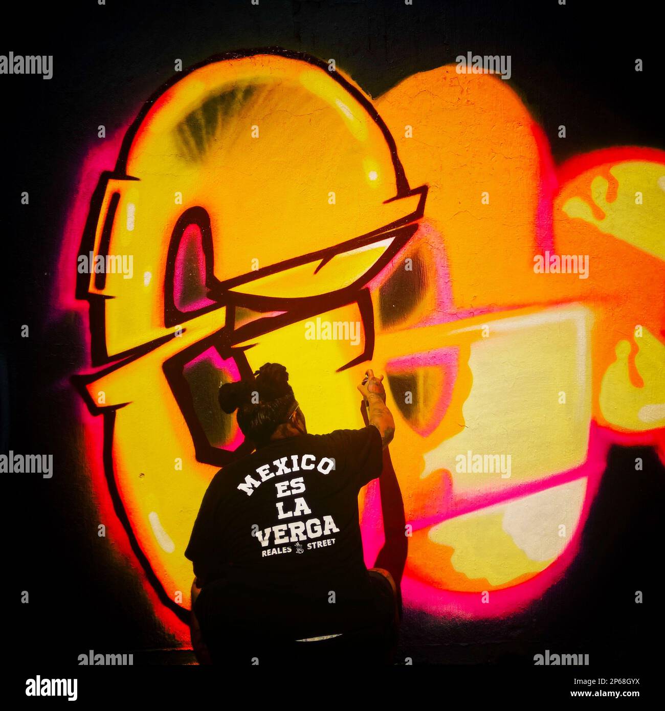 A Mexican street artist paints graffiti on the wall of a cemetery