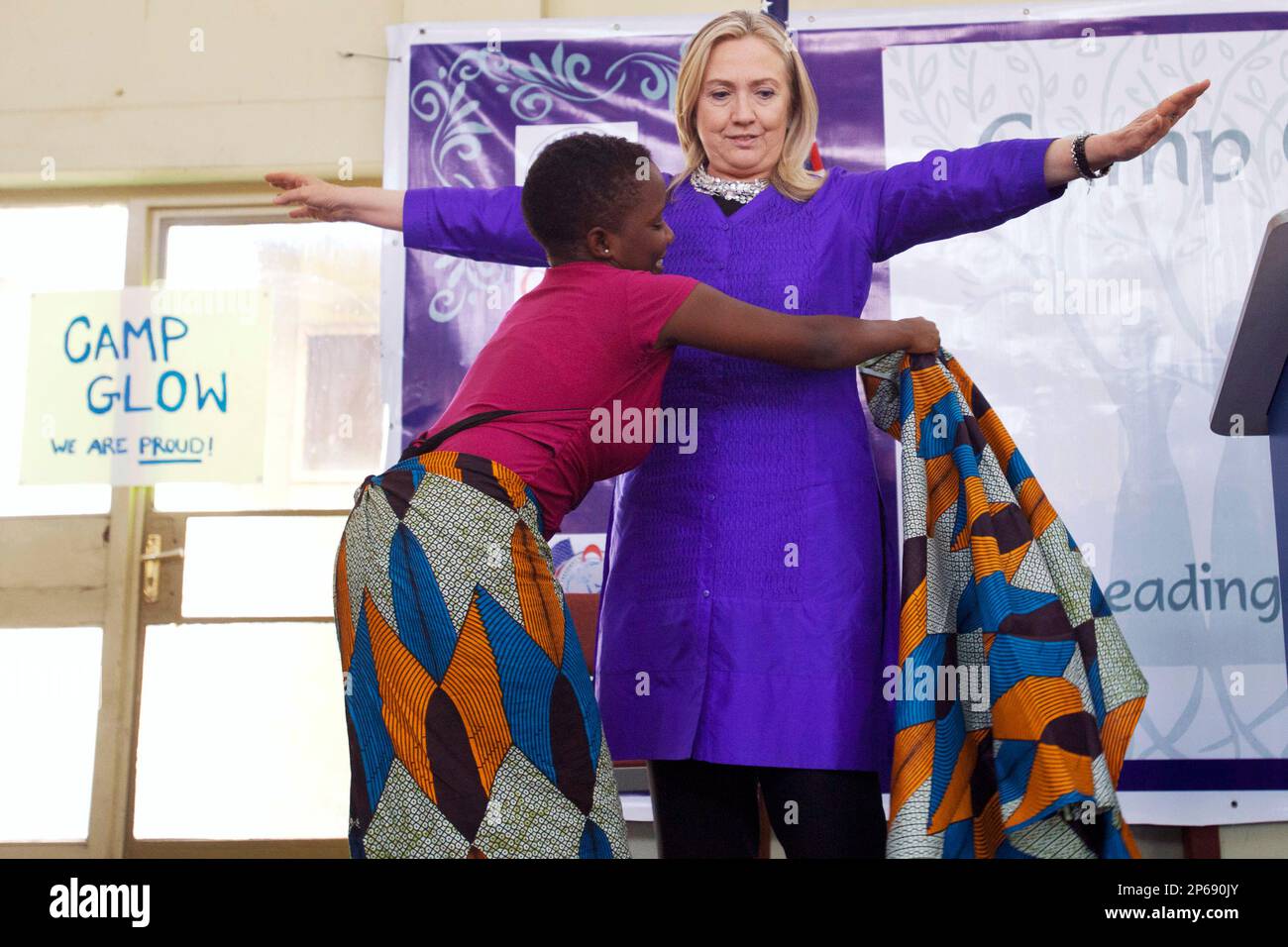 Triza Lapani helps U.S. Secretary of State Hillary Rodham Clinton to put on  a chitenje cloth, a type of traditional skirt, at Camp Girls Leading Our  World (GLOW) run by the Peace
