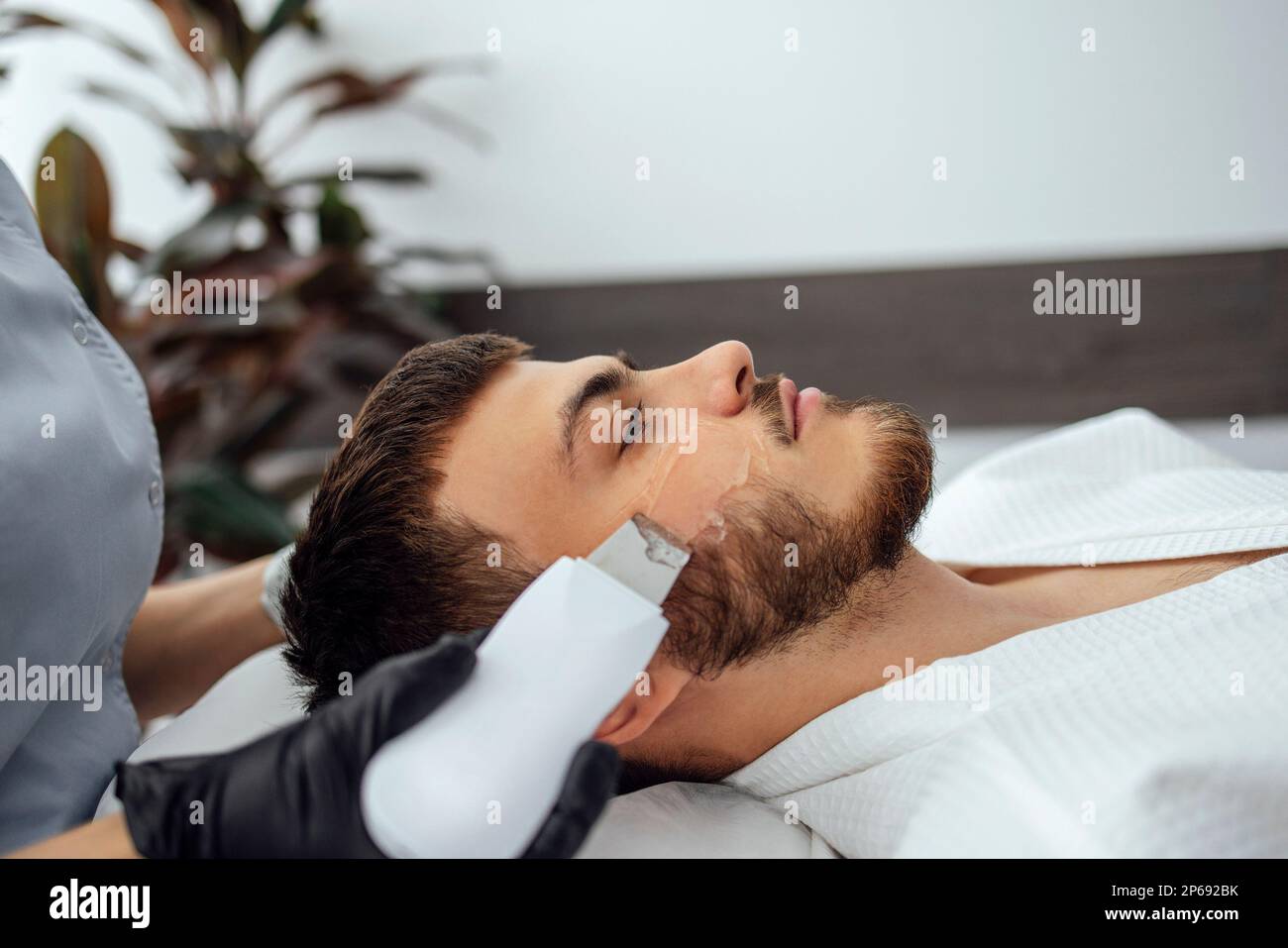 Beauty master makes ultrasonic facial peeling to her client. Youngcaucasian man doing an effective cleansing of the skin and pores in a beauty salon. Stock Photo