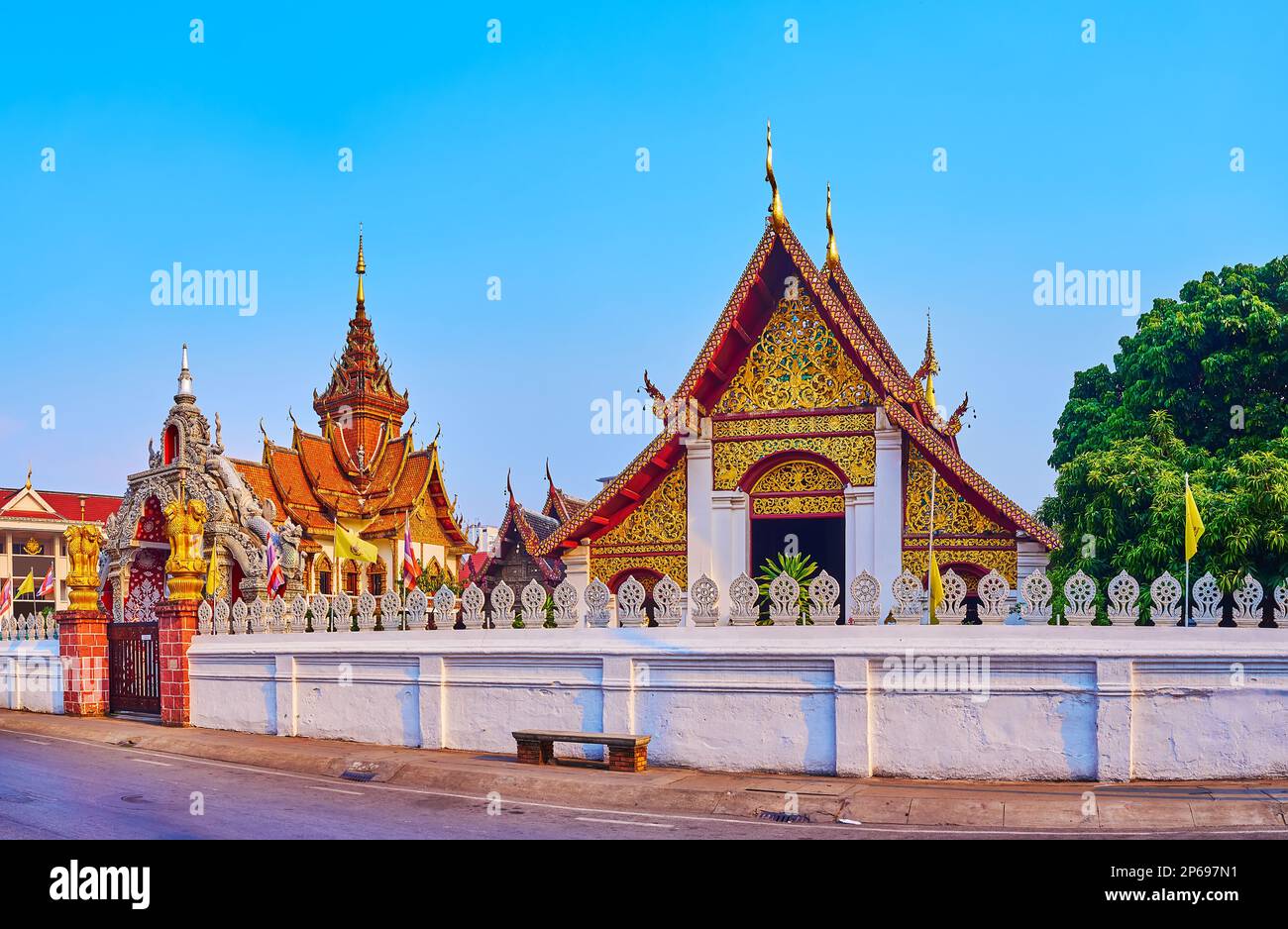 The beautiful gable ends and multi-tired roofs of the shrines of Wat Buppharam behind the white sculptured fence, Chiang Mai, Thailand Stock Photo