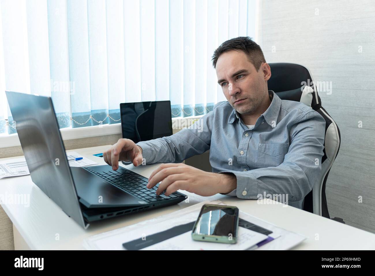 He is using touchpad while reading an e-mail on laptop . Multi-tasking businessman working in the office. Stock Photo