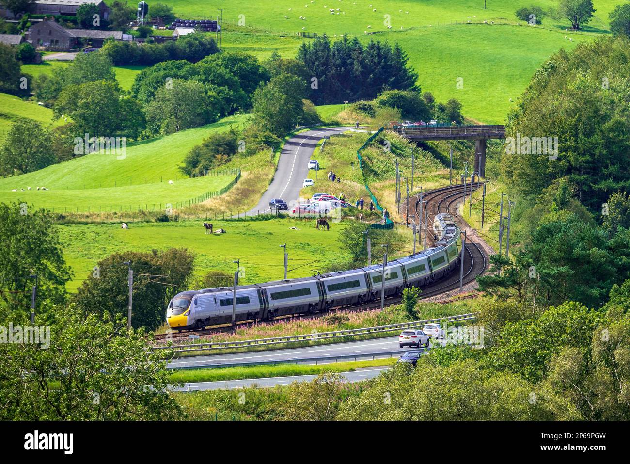 An Avantini Pendolino tilting train seen on the curves onThe West Coast mainline at Beck foot near Tebay, with the M6 running alongside. Stock Photo