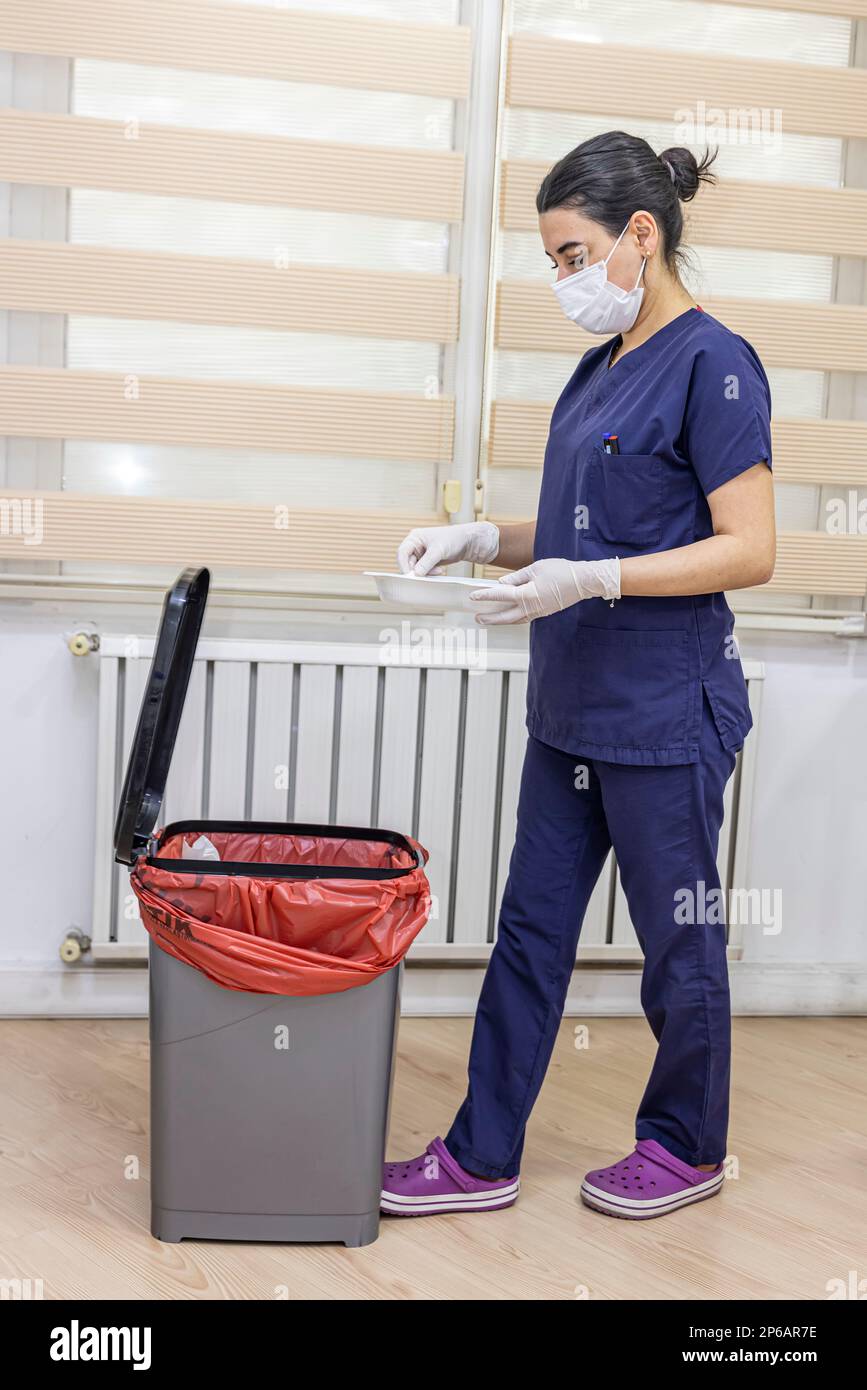 Nurse throws medical garbage into Medical waste bin in office. A female nurse holding a red garbage bag. Maid and infection trash in hospital. Infecti Stock Photo