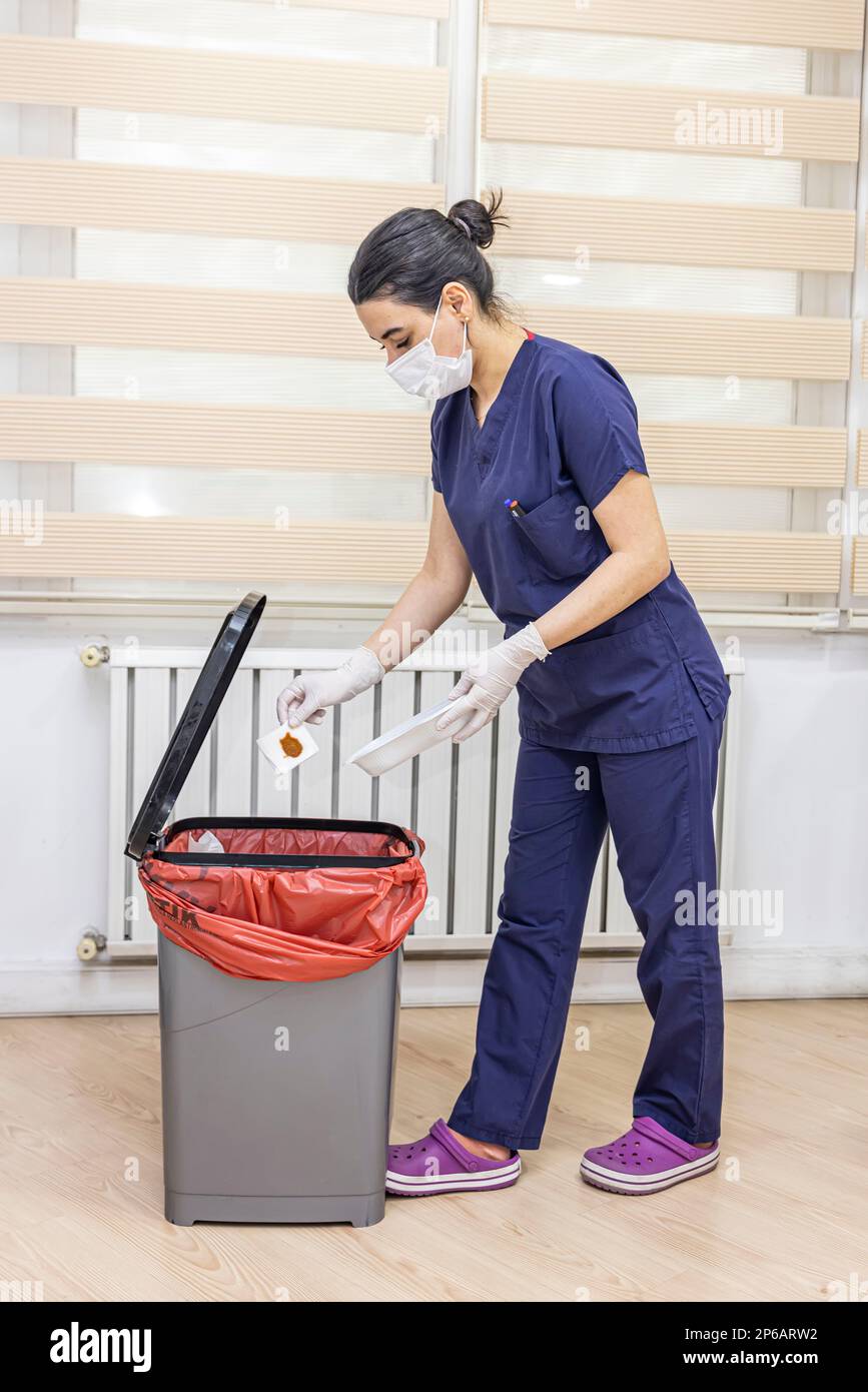 Nurse throws medical garbage into Medical waste bin in office. A female nurse holding a red garbage bag. Maid and infection trash in hospital. Infecti Stock Photo