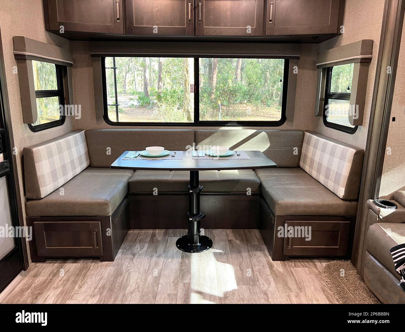 Perfect for remote work, the modern, clean design of this fifth wheel travel trailer shows the dining area with storage and a huge picture window. Stock Photo