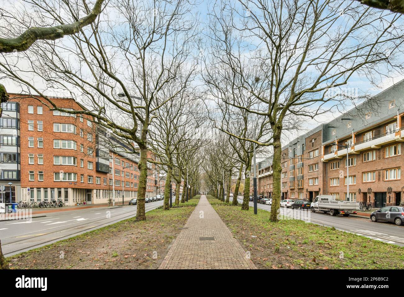 Amsterdam, Netherlands - 10 April, 2021: a tree lined street with cars parked on both sides and trees in the middle of the road to the right Stock Photo