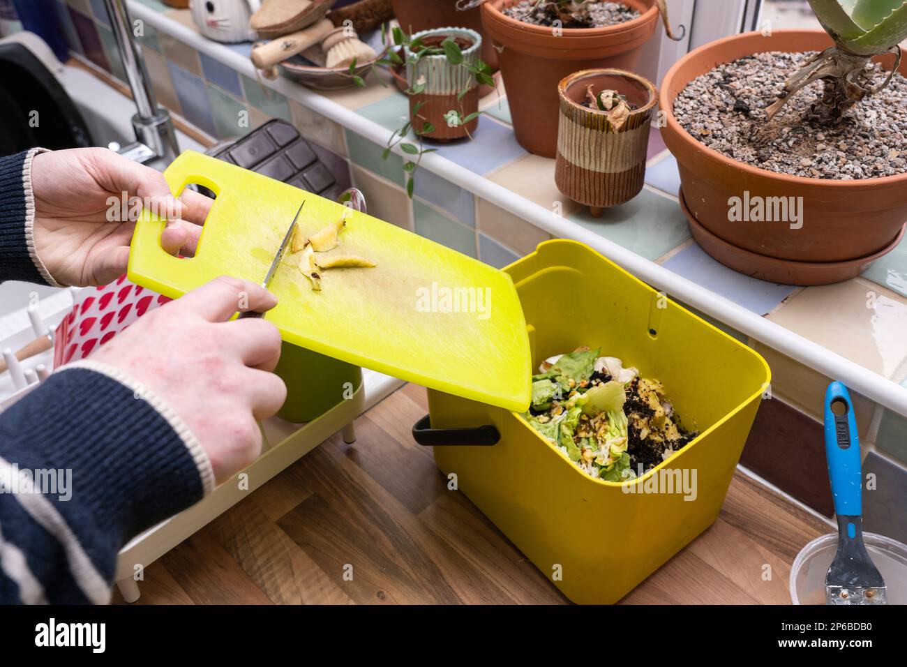 Man pushing food waste from a chopping board into a food recycling bin in a domestic kitchen, ready for composting, UK. Theme: sustainability at home Stock Photo