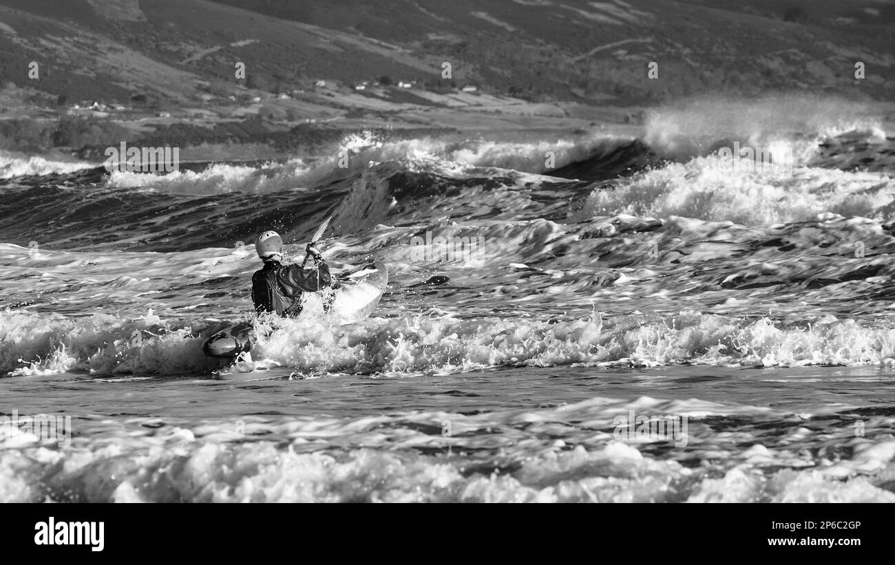 Kayaker paddling out towards heavy surf off Brora beach Stock Photo
