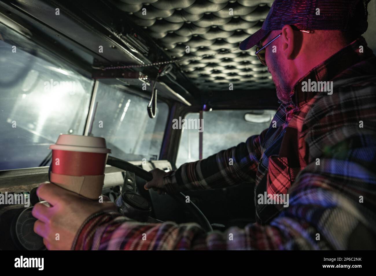 Night Time Semi Truck Driving. Caucasian Trucker Driving and Drinking Fresh Hot Coffee To Get Some Caffeine Boost. Stock Photo
