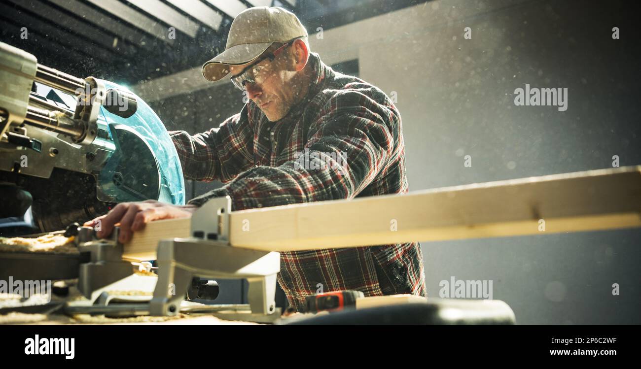 Woodworker General Construction Contractor Behind Powerful Wood Saw. Cutting Beams to Size. Panoramic Photo. Stock Photo