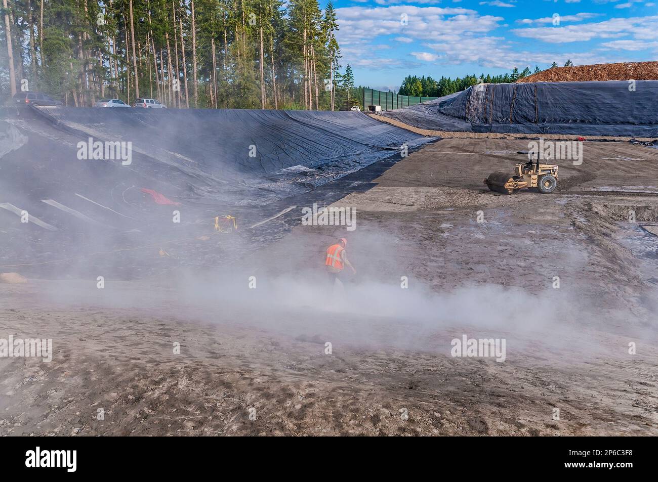 A worker walks through gel powder cloud in areas of excavation and plastic geomembrane coverings at an active landfill. Stock Photo