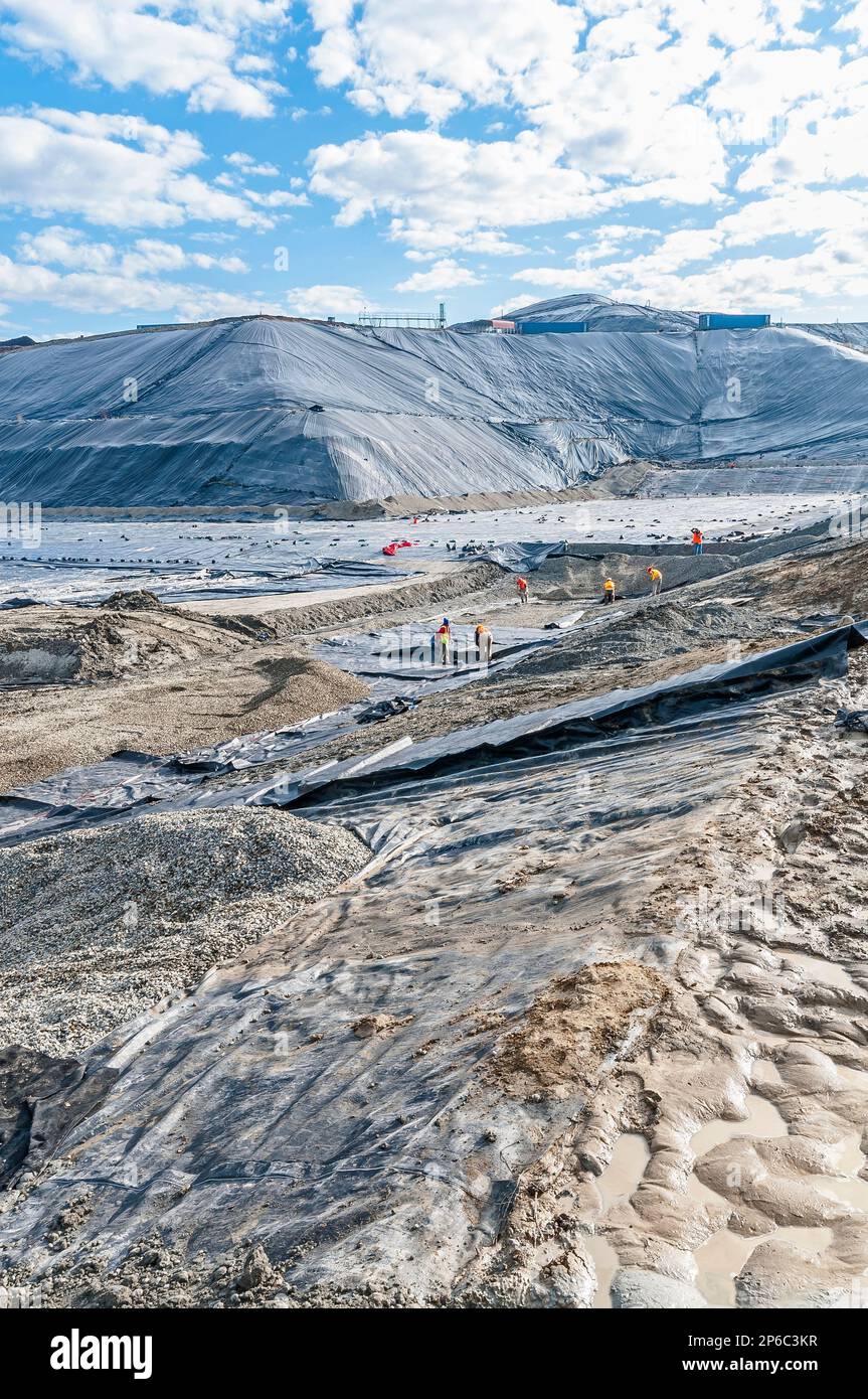 Workers in vast areas of excavation and plastic geomembrane coverings at an active landfill. Stock Photo