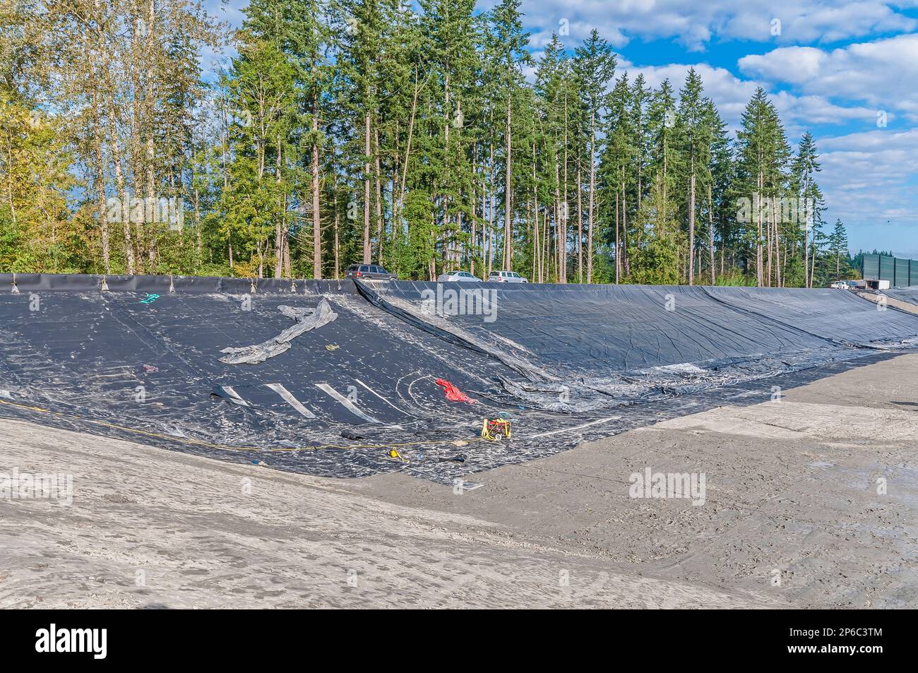 A covered hillside and a portable generator in an area of excavation and plastic geomembrane coverings at an active landfill. Stock Photo