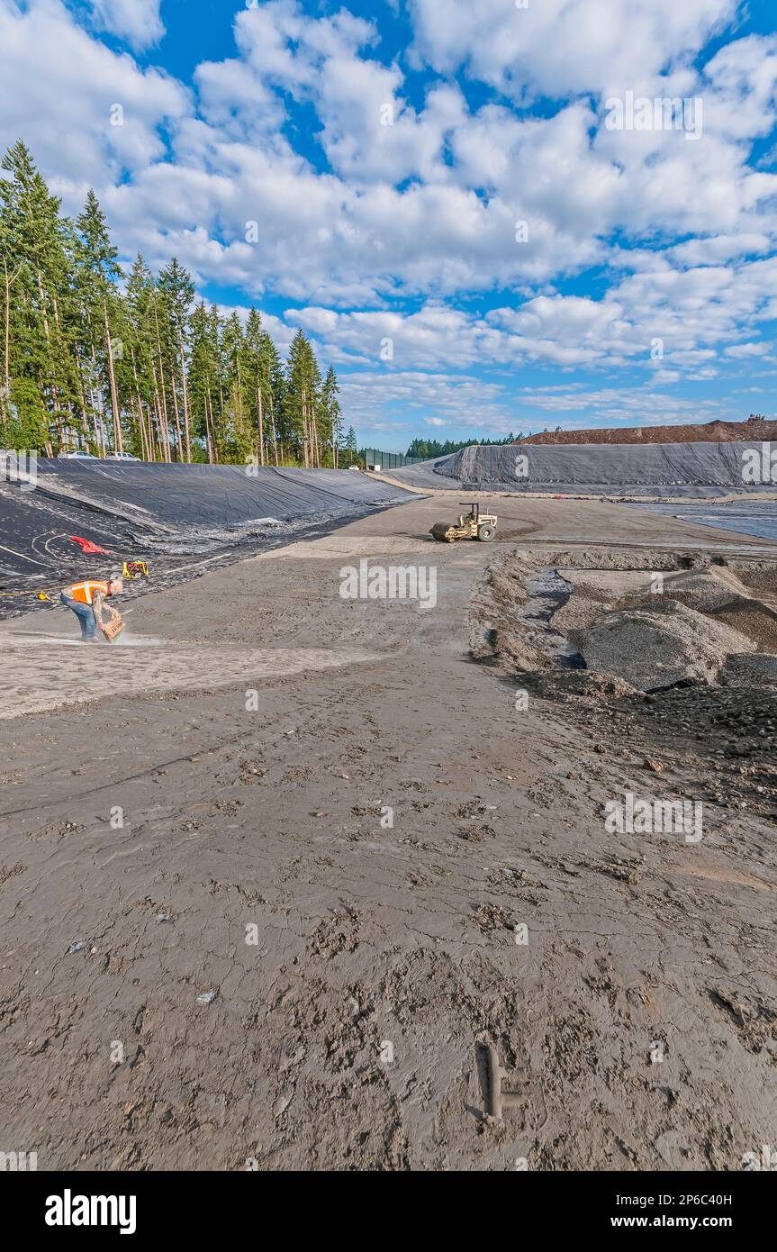 A worker pours gel powder from bag in areas of excavation and plastic geomembrane coverings at an active landfill. Stock Photo