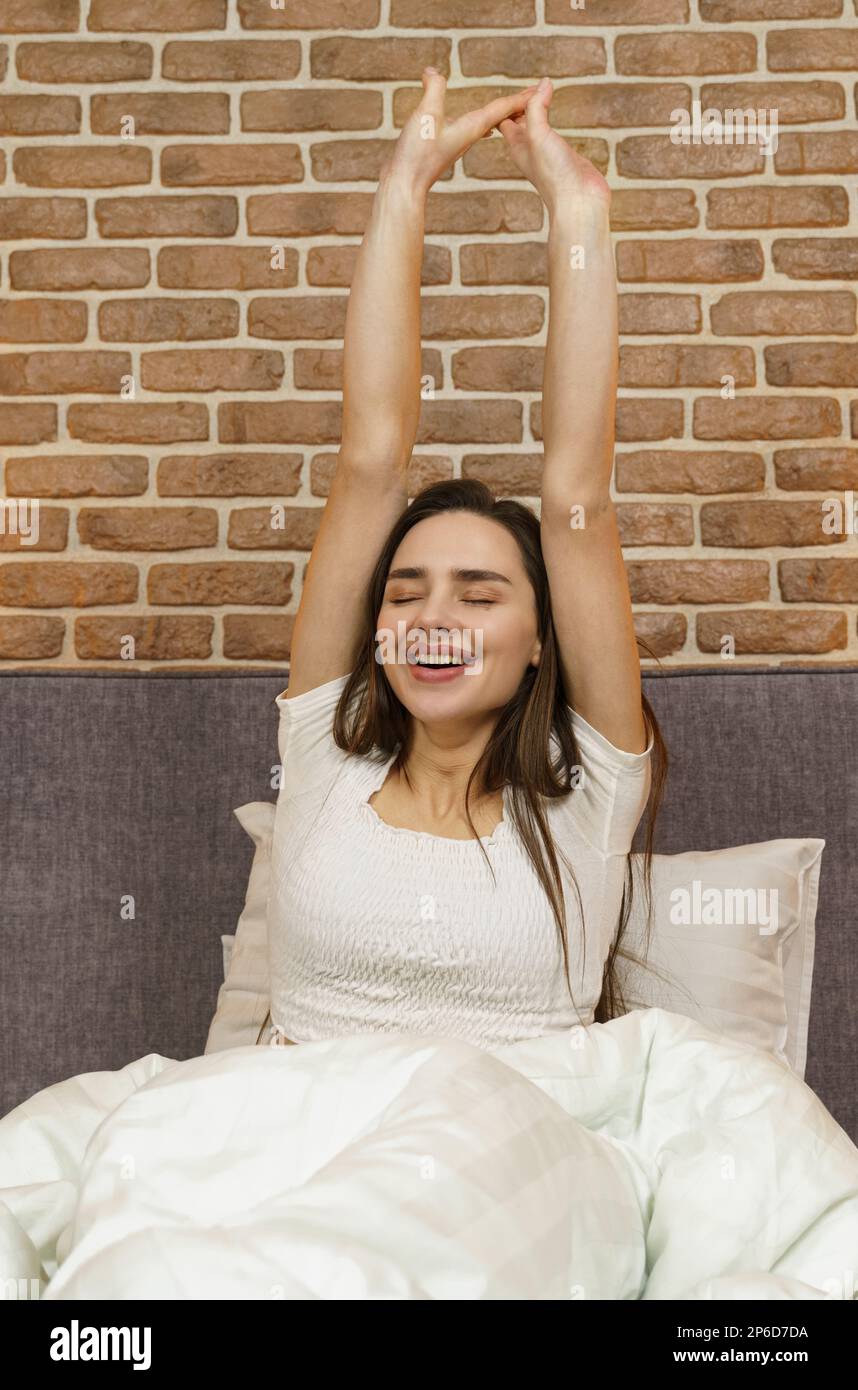 Beautiful woman sits on the bed, stretches her arms up after sleeping