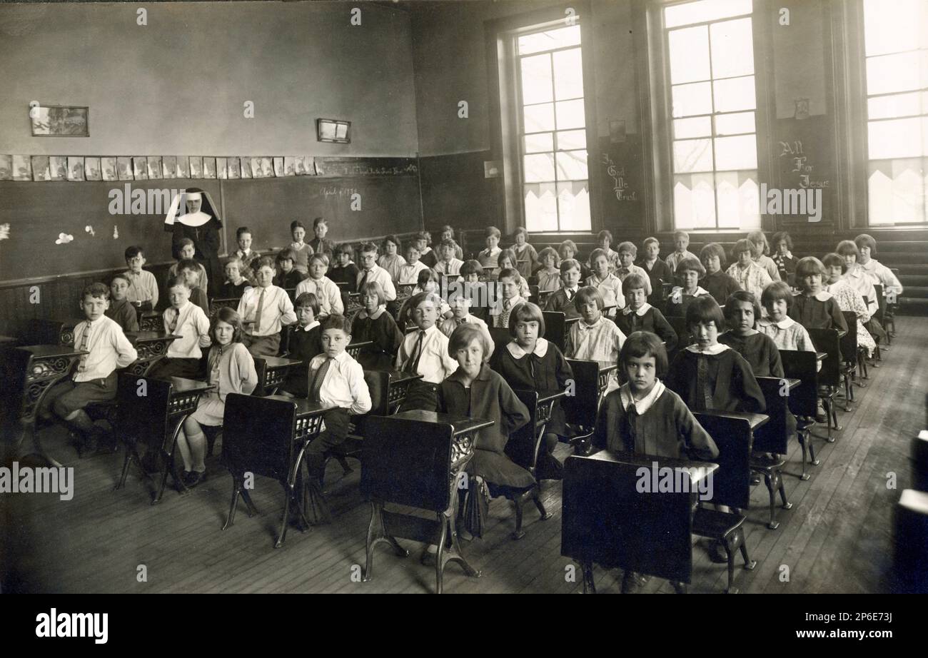 Old Catholic School Classroom Interior, Children Seated at Desks with Hands Behind their Backs, Nun in Habit, Religious School,  1930 Stock Photo