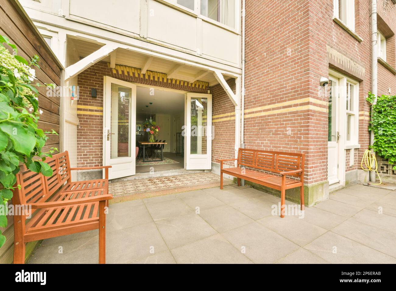 two wooden benches in front of a brick building with green plants on ...
