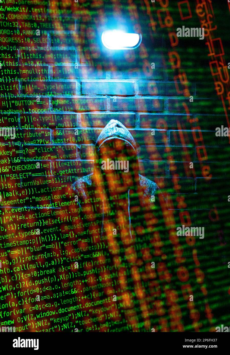 A hacker in a hoodie behind lines of code Stock Photo