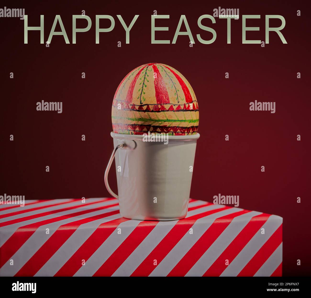 Hand painted Easter egg on a striped box with a red gradient background. Stock Photo