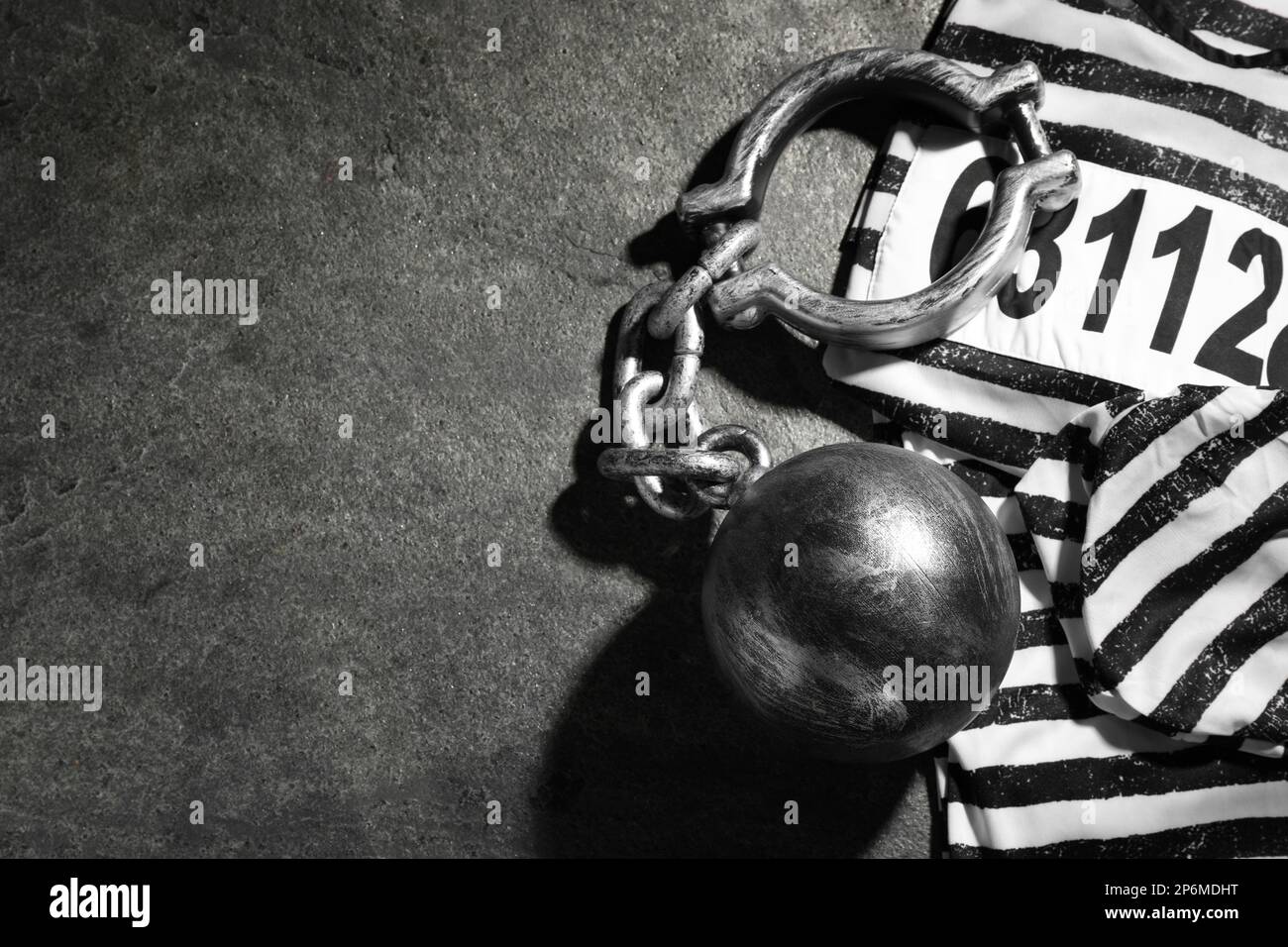 Prisoner ball with chain and jail clothes on grey table, flat lay