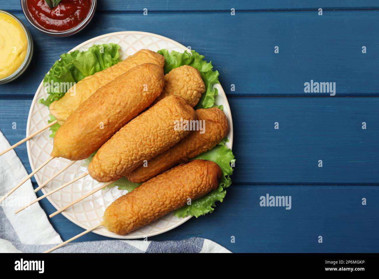 Delicious deep fried corn dogs and sauces on blue wooden table, flat lay. Space for text Stock