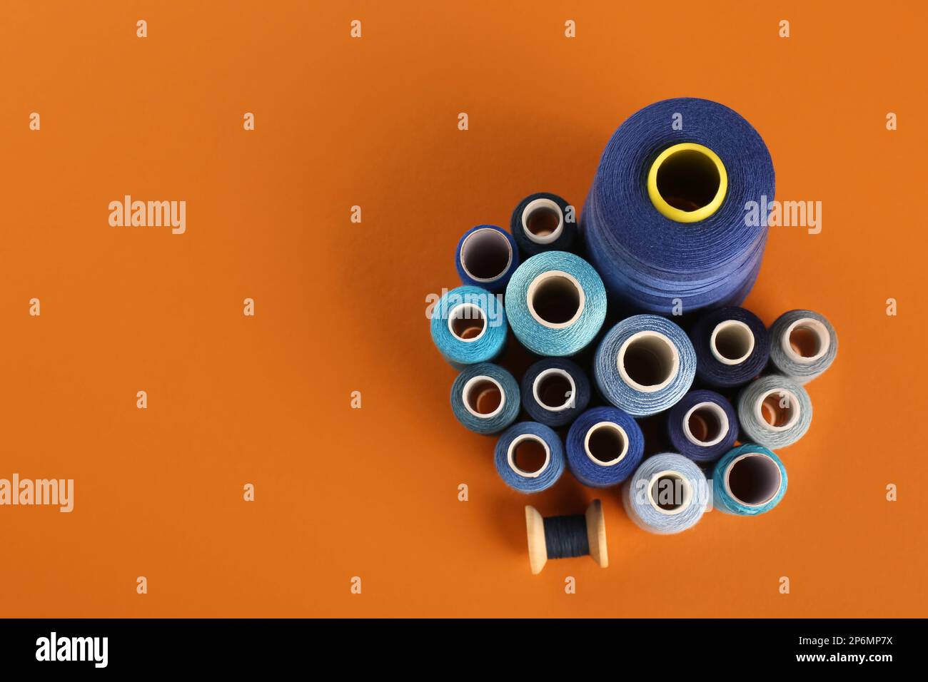 Different shades of blue sewing threads on orange background, flat lay