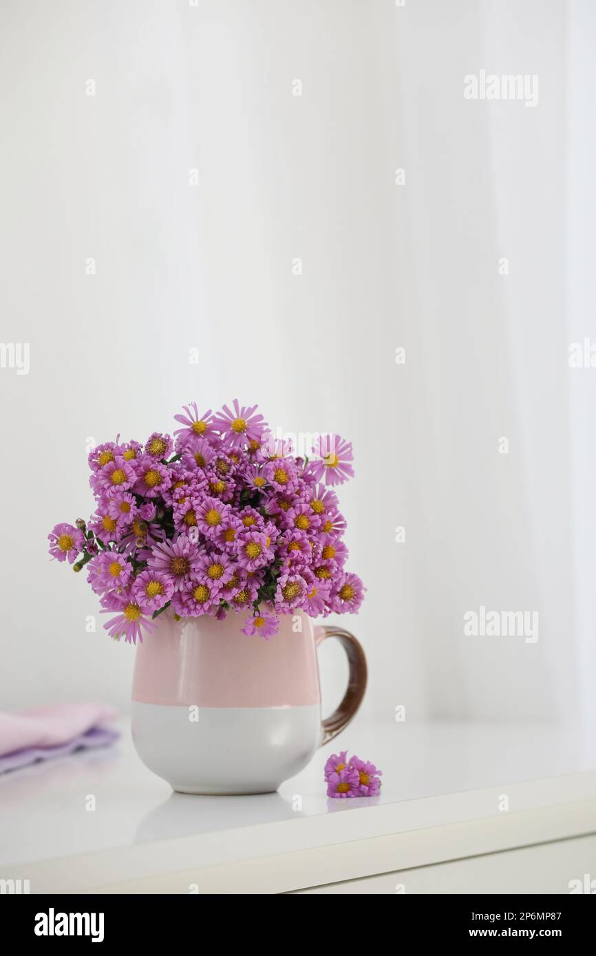 Cup with beautiful flowers on white table in light room Stock Photo