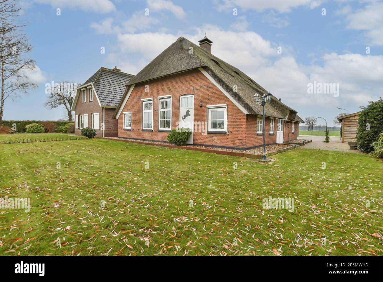 a red brick house with thatched roof and white trim around the windows, on a grassy lawn in front of it Stock Photo