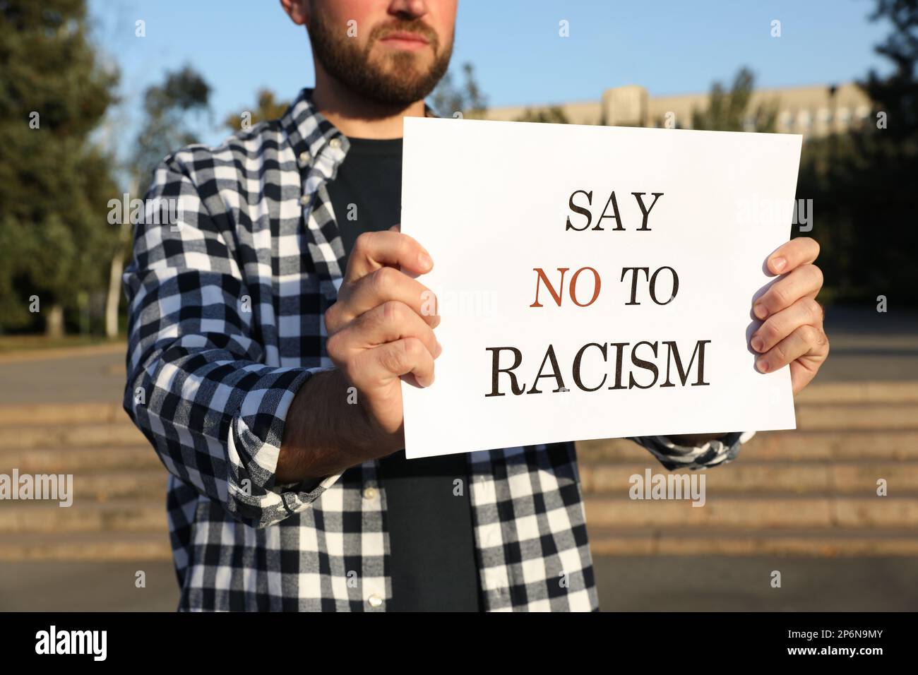 Young man holding sign with phrase Say No To Racism outdoors, closeup Stock Photo