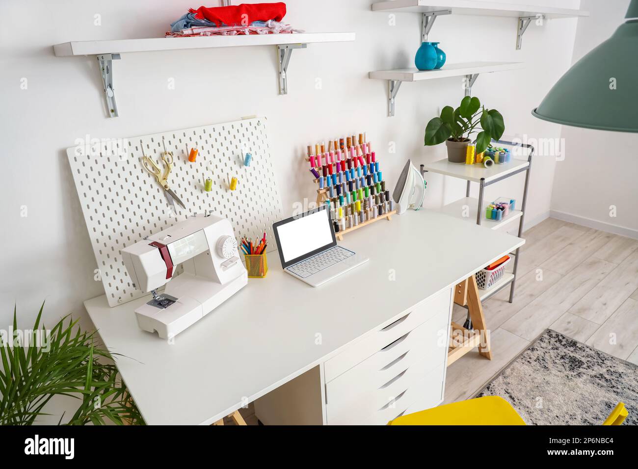 Tailor's workplace with laptop, sewing machine and pegboard in atelier ...