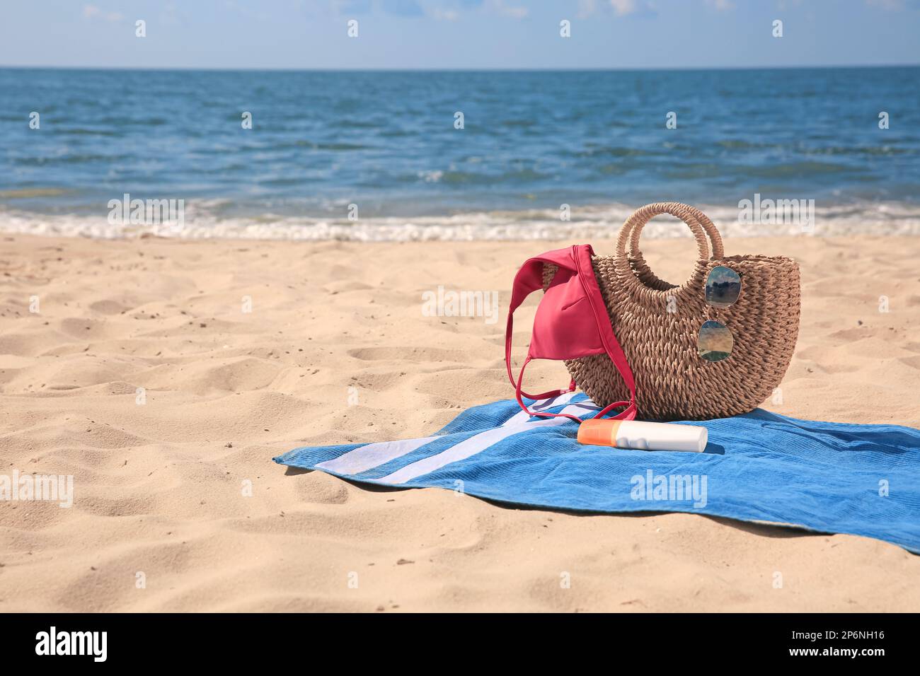 Blue striped beach towel with bag, swimsuit and accessories on sandy ...