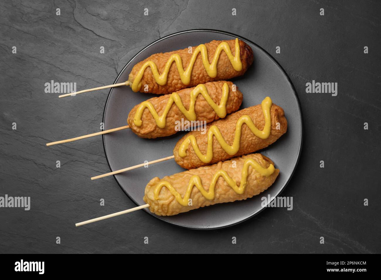 Delicious deep fried corn dogs with mustard on black table, top view