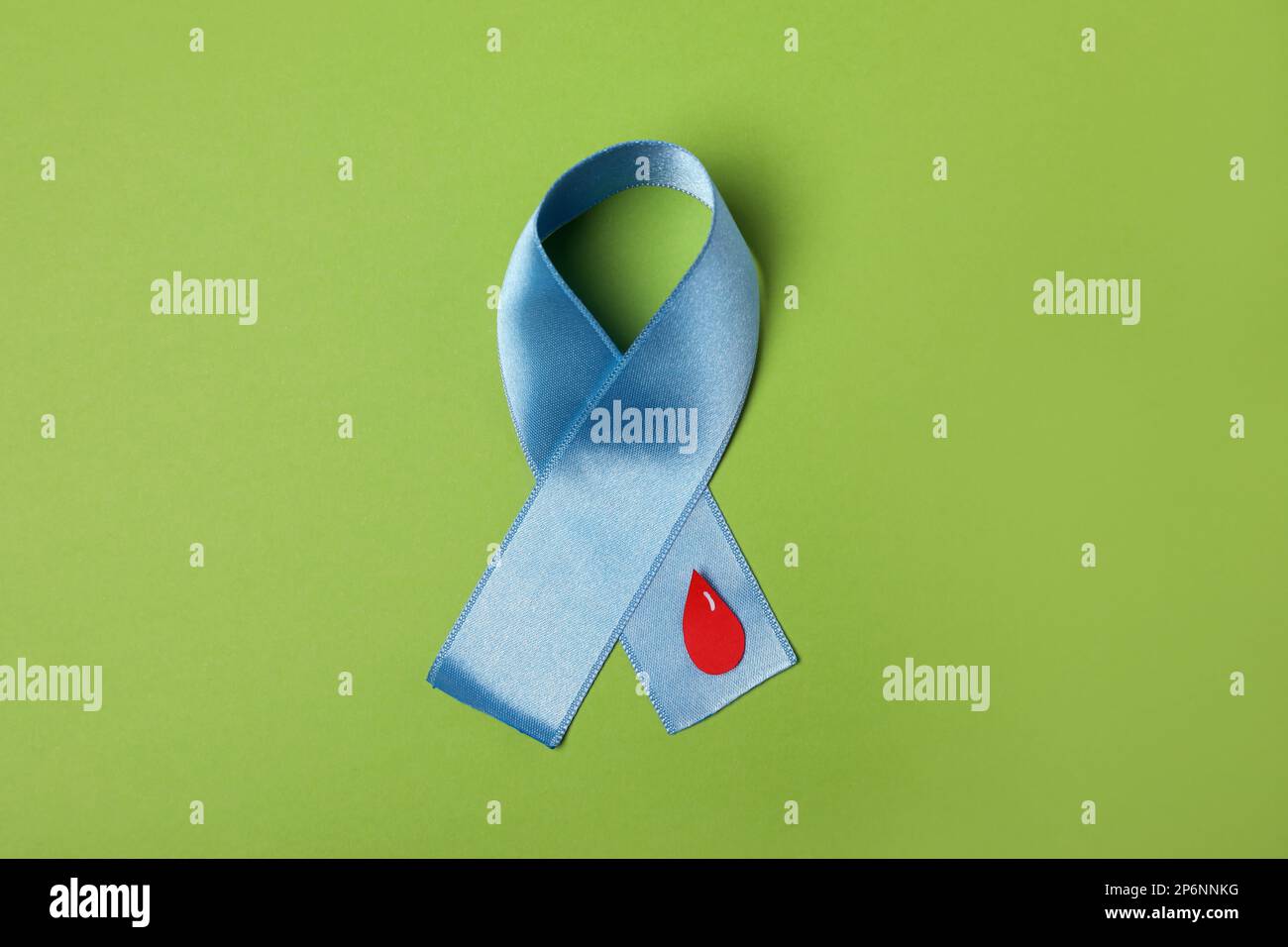 Light blue ribbon with paper blood drop on green background, top view