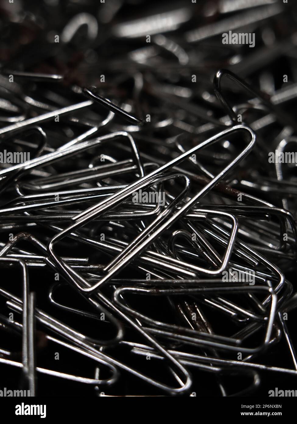 closeup macro shot of a large pile of triangular shaped shiny silver paper clips used for business or educational purposes randomly spread around Stock Photo