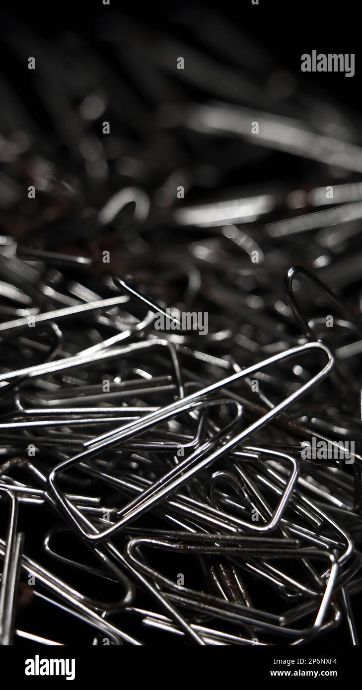 closeup macro shot of a large pile of triangular shaped shiny silver paper clips used for business or educational purposes randomly spread around Stock Photo