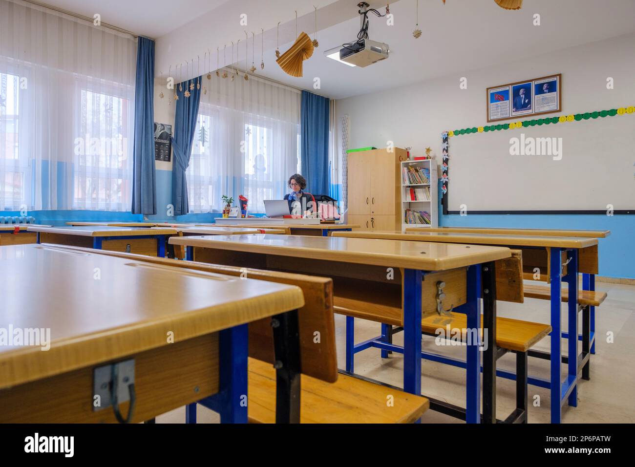 Female teacher sitting and writing notes in her notebook in empty classroom. Lots of empty desk in front of her. Horizontal indoors shot, copy space Stock Photo