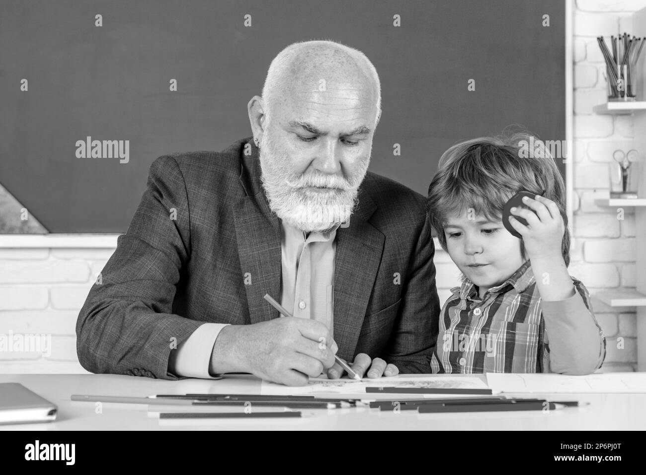 Professor and pupil in classroom at the elementary school. Child at school lesson with senior teacher. Pupil study at school with old teacher. Stock Photo