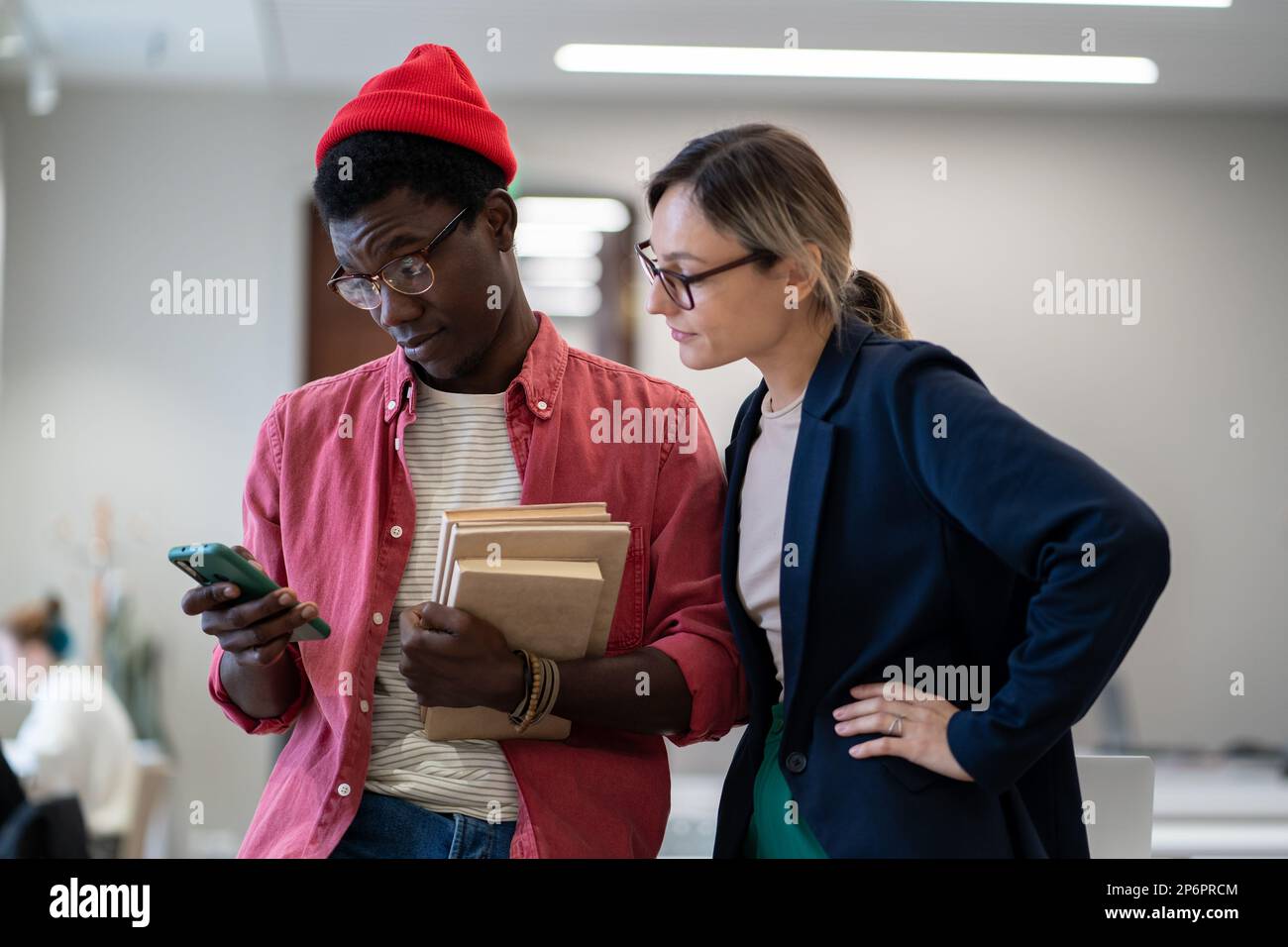 Two diverse students standing in classroom using smartphone during study break Stock Photo