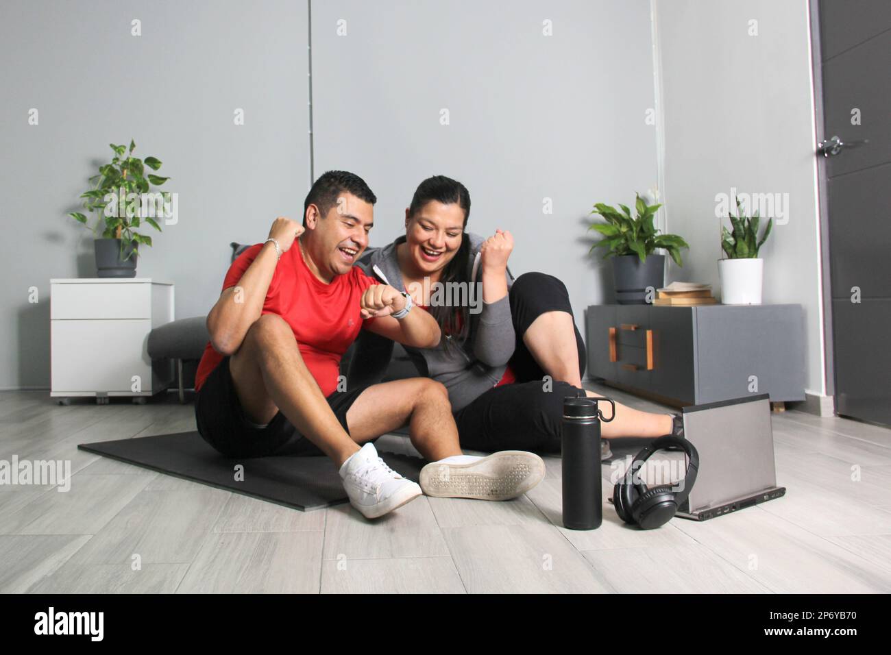 Latino adult couple of man and woman exercise at home taking online class they see the laptop in their living room together they exercise Stock Photo