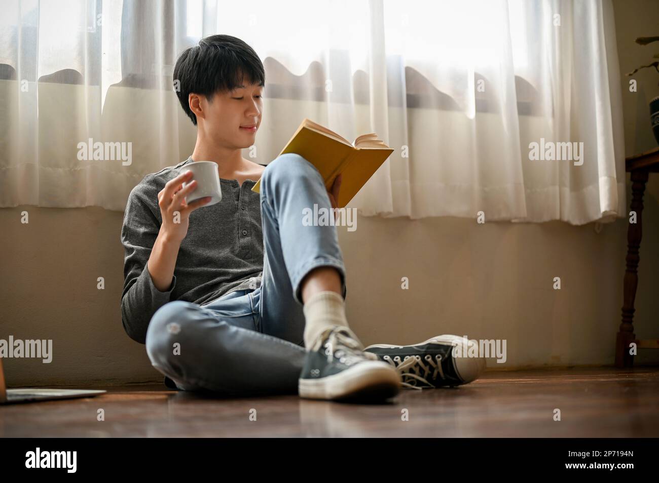 Smart and happy young Asian male college student in casual clothes sits ...