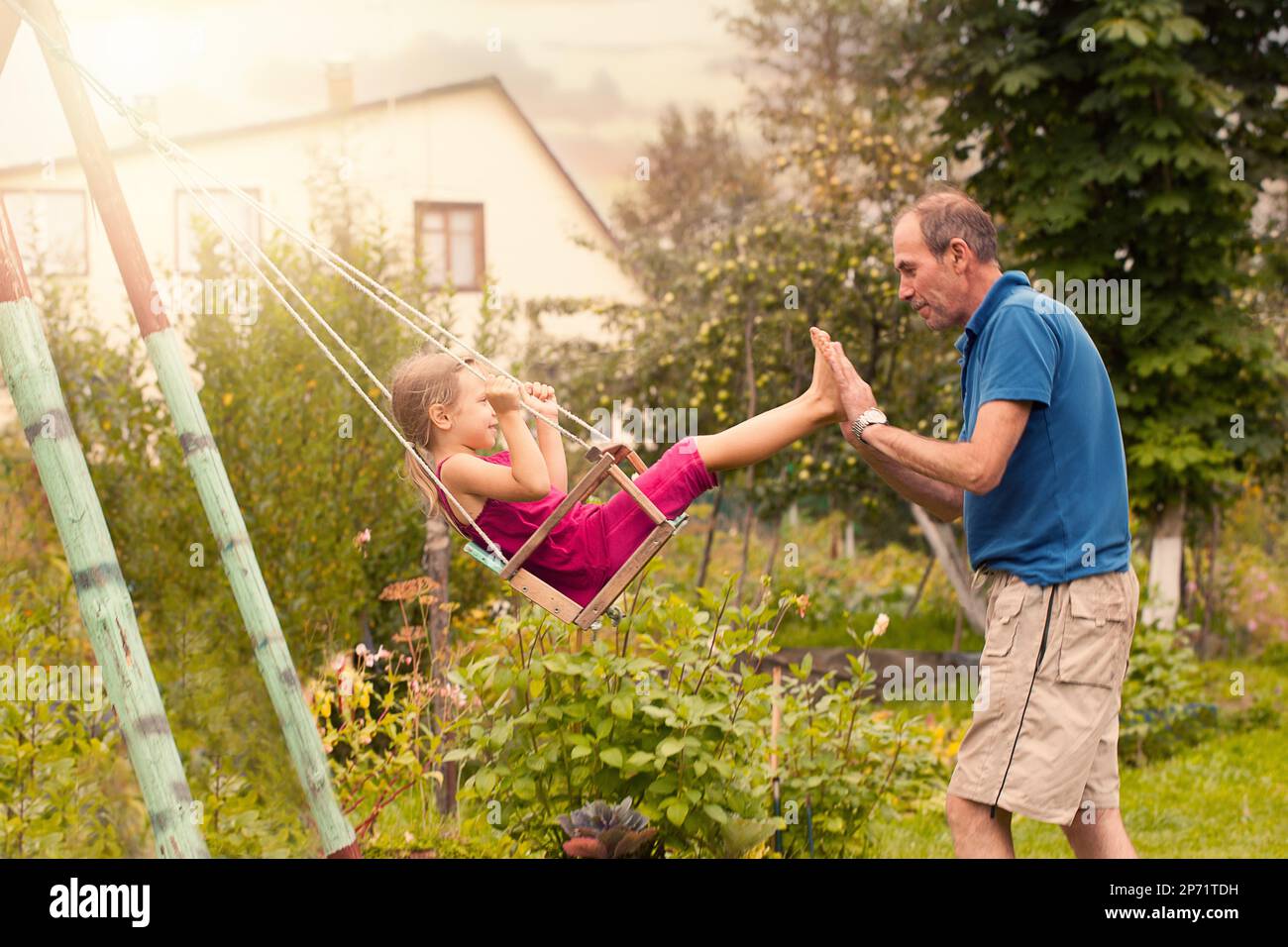 Cute little girl on a swing. Smiling child playing with Grandpa outdoors in summer Stock Photo