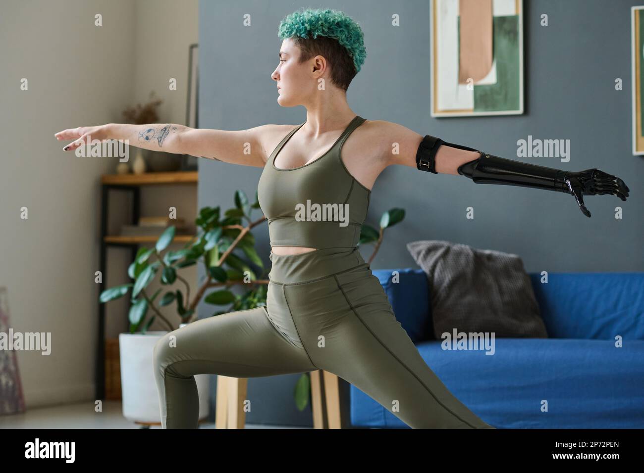 Young woman with prosthetic arm doing stretching exercises during morning training at home Stock Photo