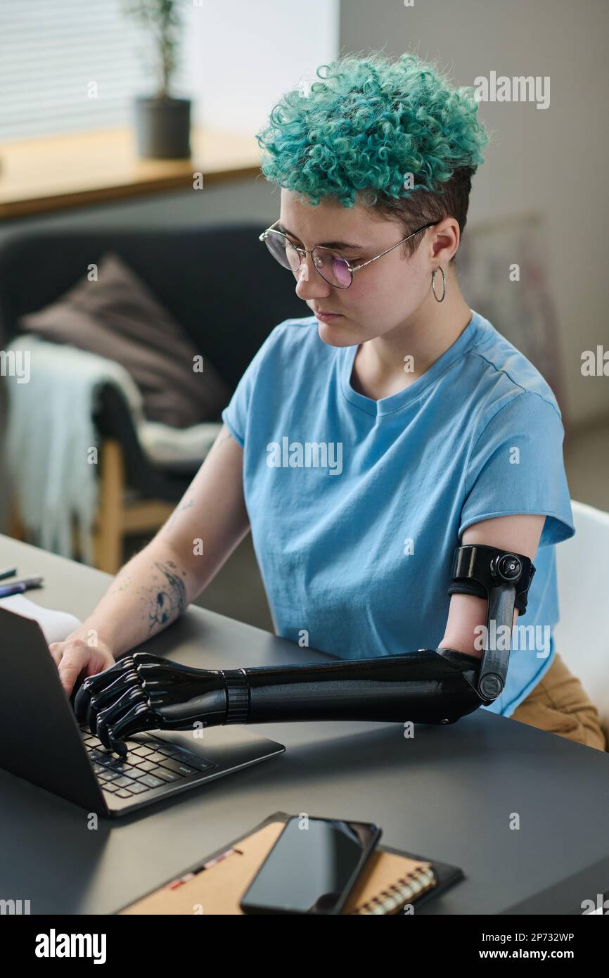 Young woman with prosthetic arm concentrating on her online work on laptop, she working at home Stock Photo