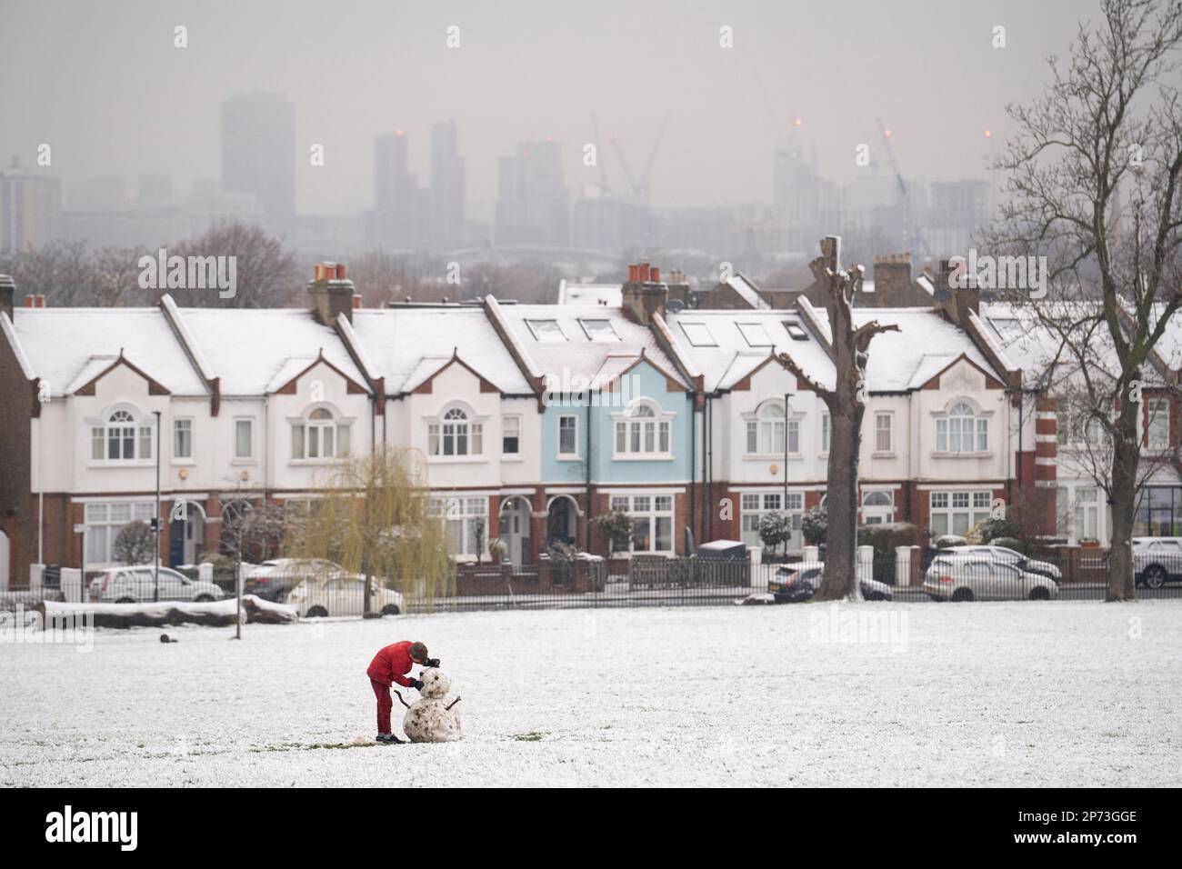 As March snow falls on south London, a boy builds a small snowman in front of period homes, in Ruskin Park, a public green space in Lambeth, on 8th March 2023, in London, England. Stock Photo