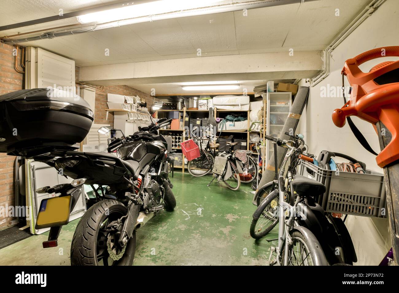 some motorcycles parked in a garage with no one on the bike, and another behind it that has been removed Stock Photo