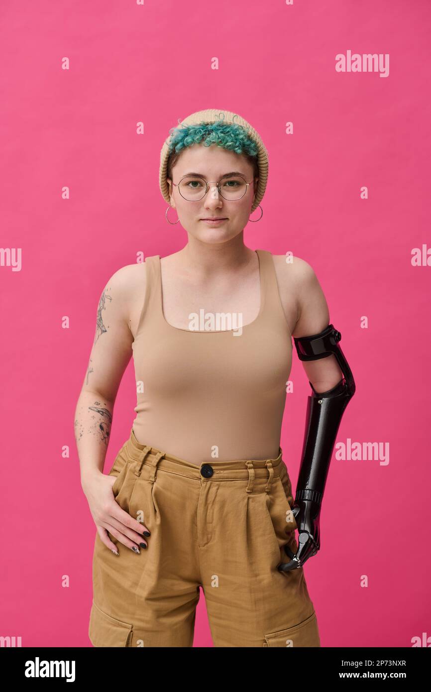 Portrait of young girl with prosthetic arm looking at camera standing against pink background Stock Photo
